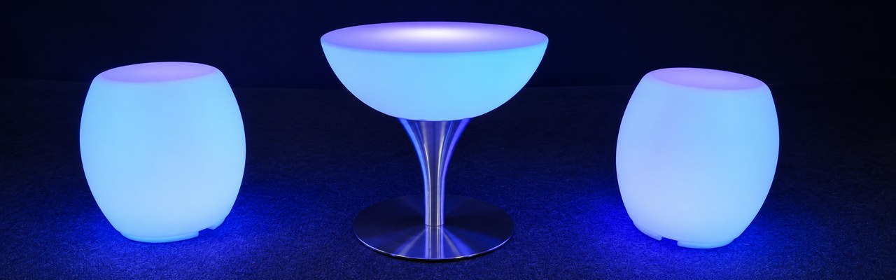 Table basse Lounge éclairée en bleu sur son pied en inox, avec deux poufs lumineux