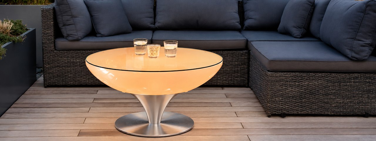 Table Lounge ambrée avec plateau transparent et pied en inox sur une terrasse