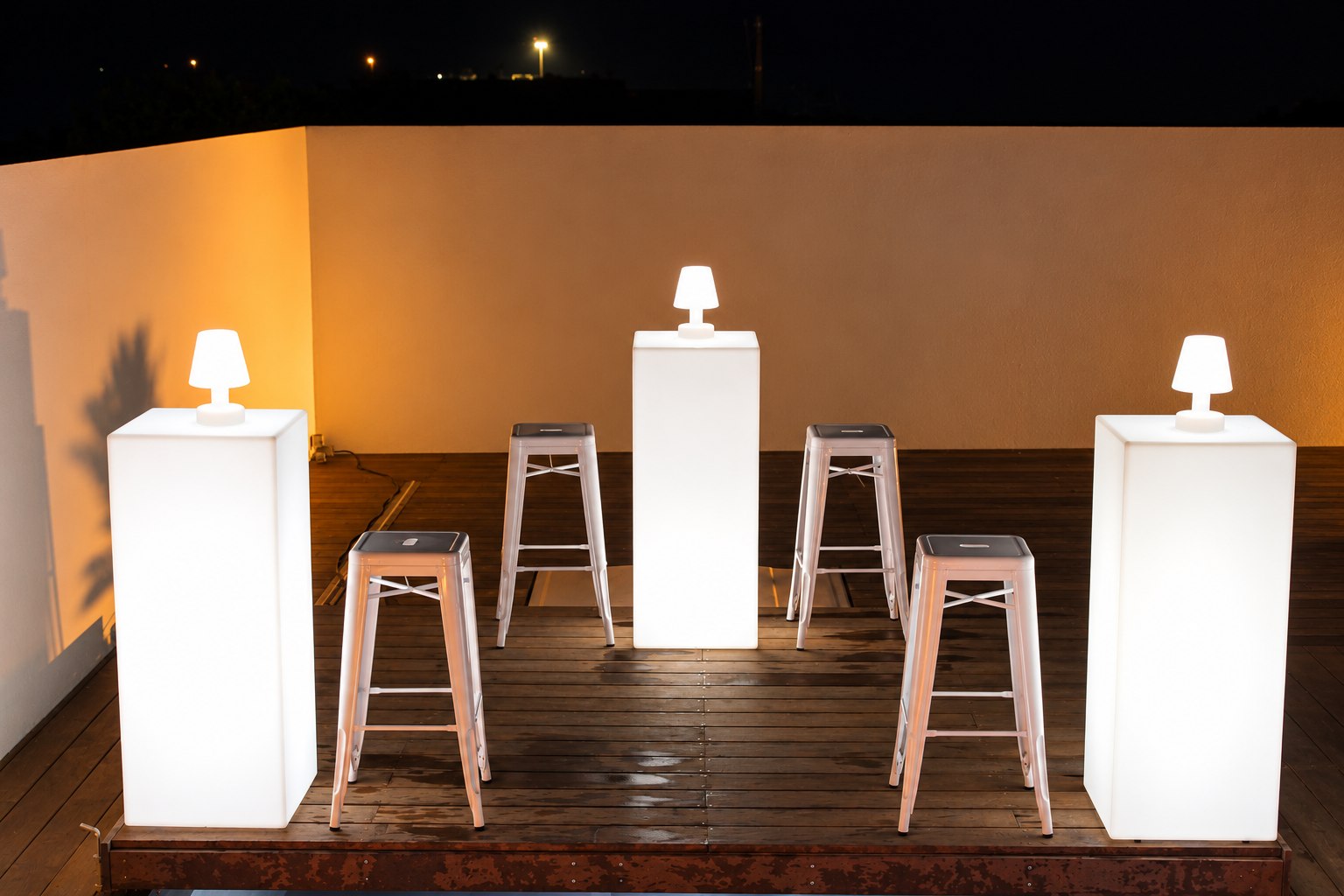 Mange-debout lumineux droits et tabourets sur une terrasse éclairée en blanc