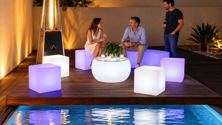 Table basse ronde blanche et cubes lumineux lavande sur une terrasse de piscine