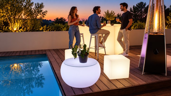 Table basse ronde, cube blanc et bar lumineux sur une terrasse au crépuscule