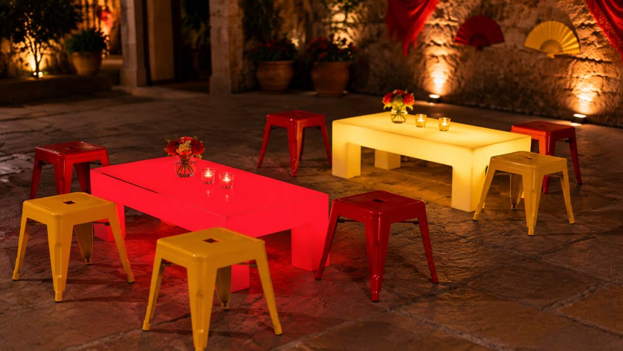 Tabourets bas acier rouges et jaunes autour de tables lumineuses