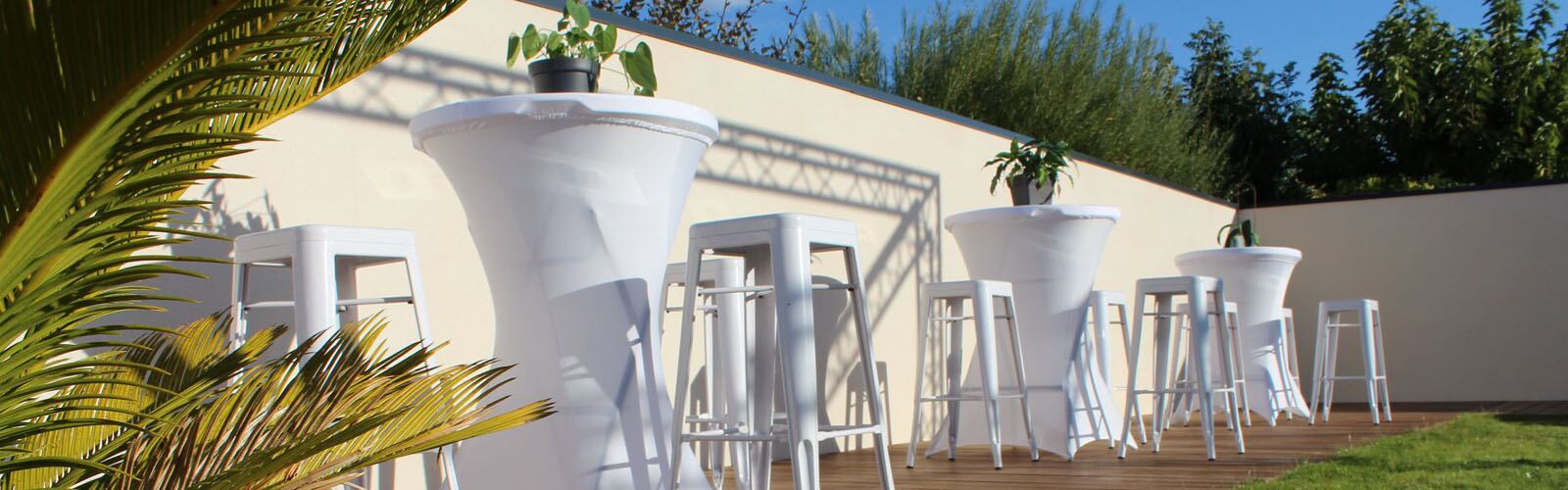 Tabourets hauts acier blancs autour de mange-debout dans un jardin ensoleillé